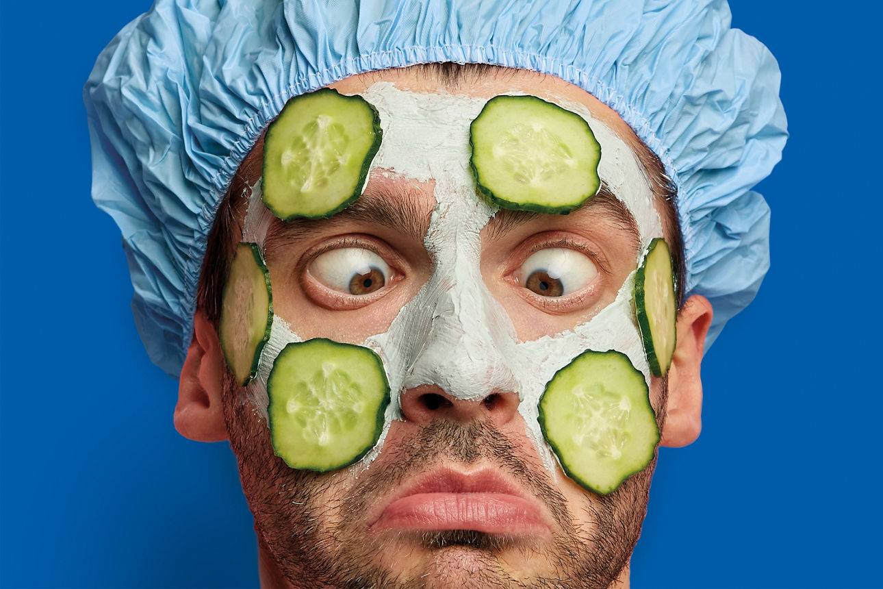 Ein Mann mit einer Gesichtsmaske und Gurkenscheiben im Gesicht schielt auf seine Nase