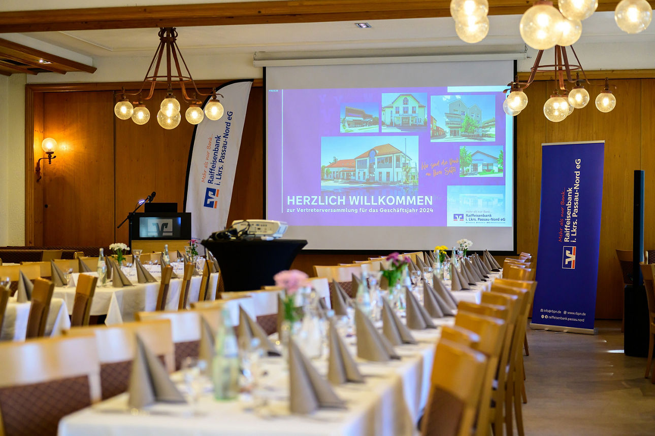 Ein Saal mit einer Leinwand und zwei langen gedeckten Tischen.