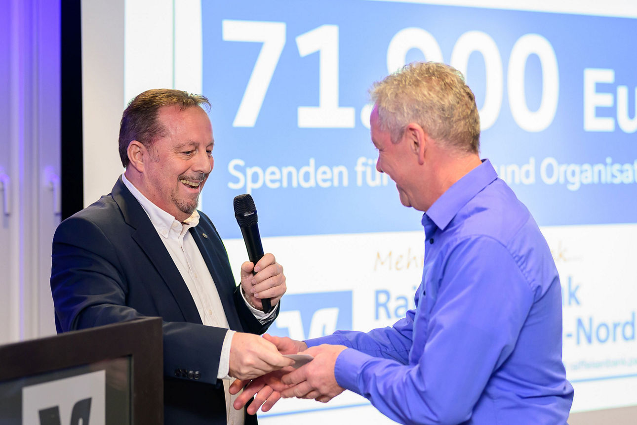 ein Mann erhält per Handschlag ein Kuvert von einem Mann.