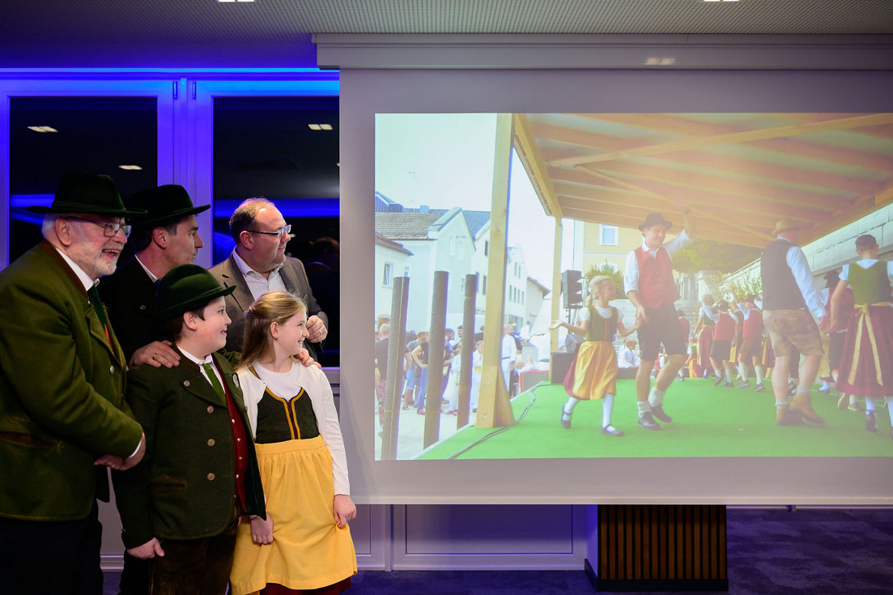 3 Erwachsende Männer, ein Junge und ein Mädchen schauen ein Video auf einer Leinwand