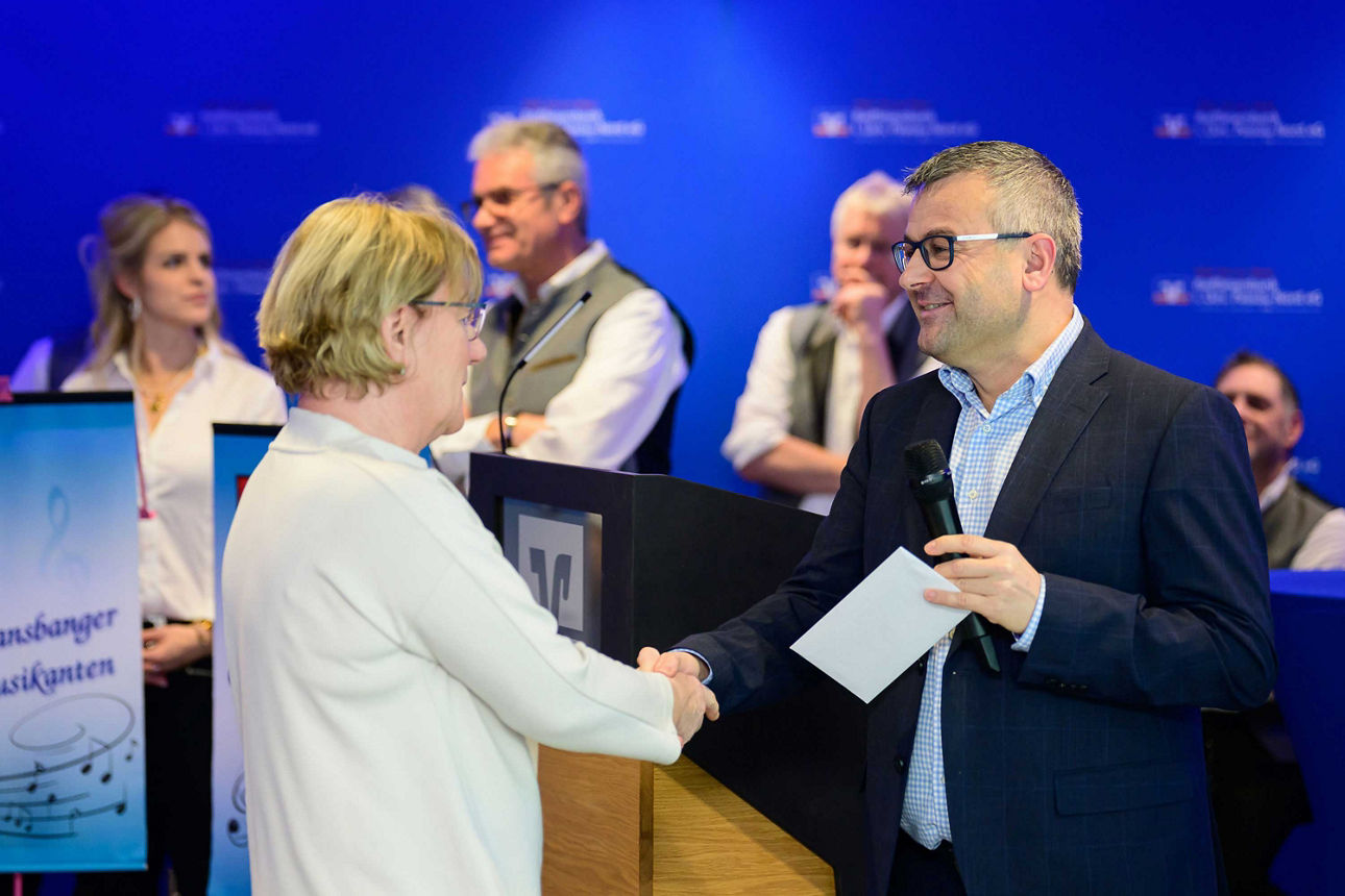 Eine Frau erhält per Handschlag ein Kuvert von einem Mann.