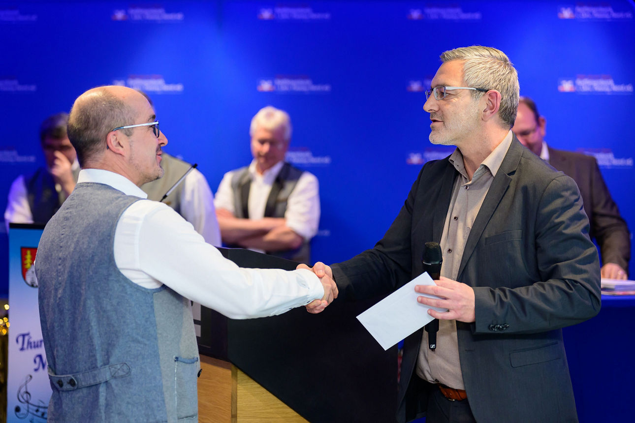 ein Mann erhält per Handschlag ein Kuvert von einem Mann.