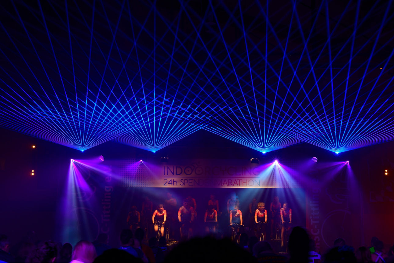 Gruppe von Menschen, die auf einer Bühne in buntem Scheinwerferlicht Indoor-Fahrrad fahren