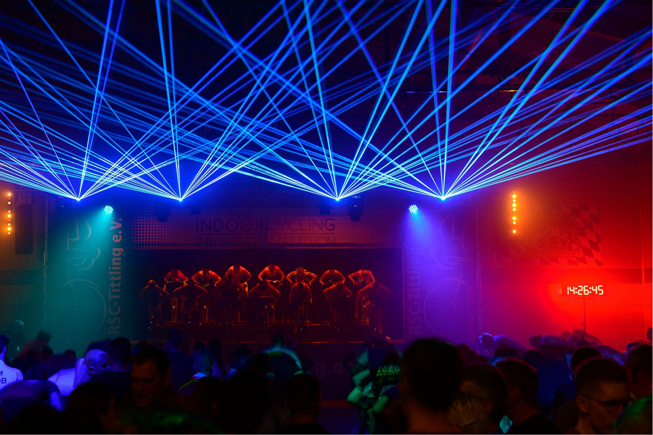 Gruppe von Menschen, die auf einer Bühne in buntem Scheinwerferlicht Indoor-Fahrrad fahren