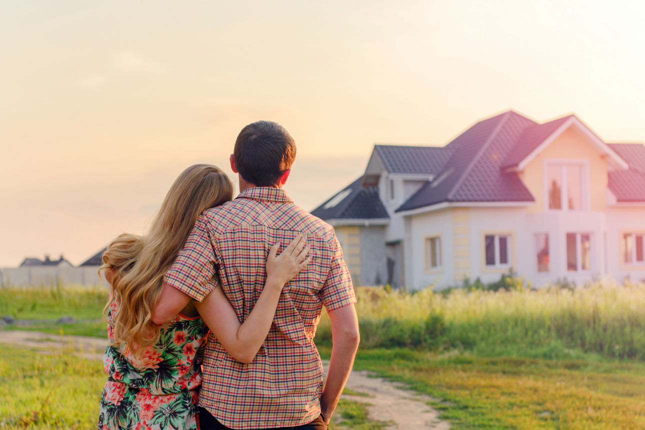 Ein Pärchen steht mit den Rücken zur Kamera und blickt auf ein Einfamilienhaus