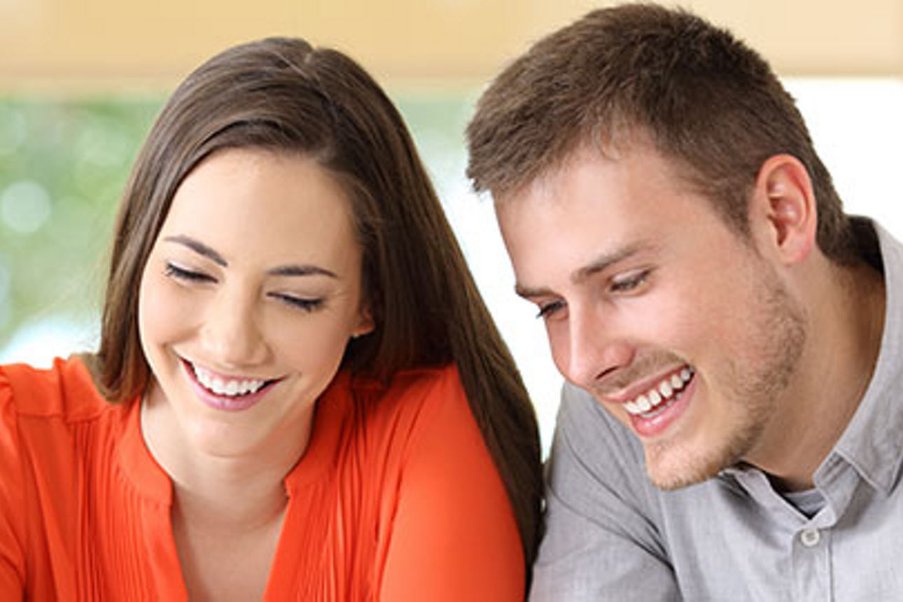 Ein Mann und eine Frau sitzen an einem Tisch und unterhalten sich mit einem fröhlichen Lächeln.