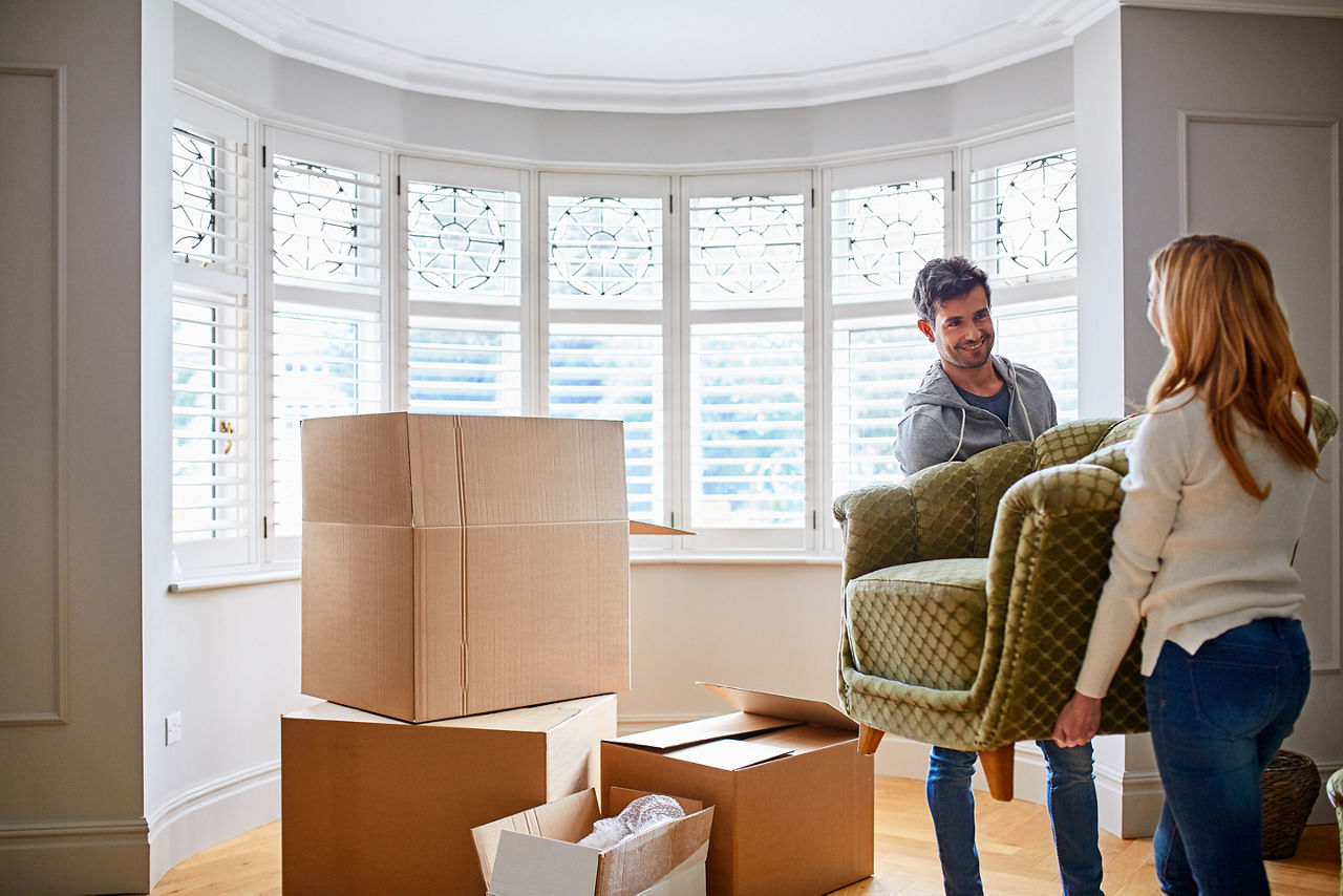Junges Pärchen zieht in eine neue Wohnung mit vielen Kisten und trägt gemeinsam ein Sofa