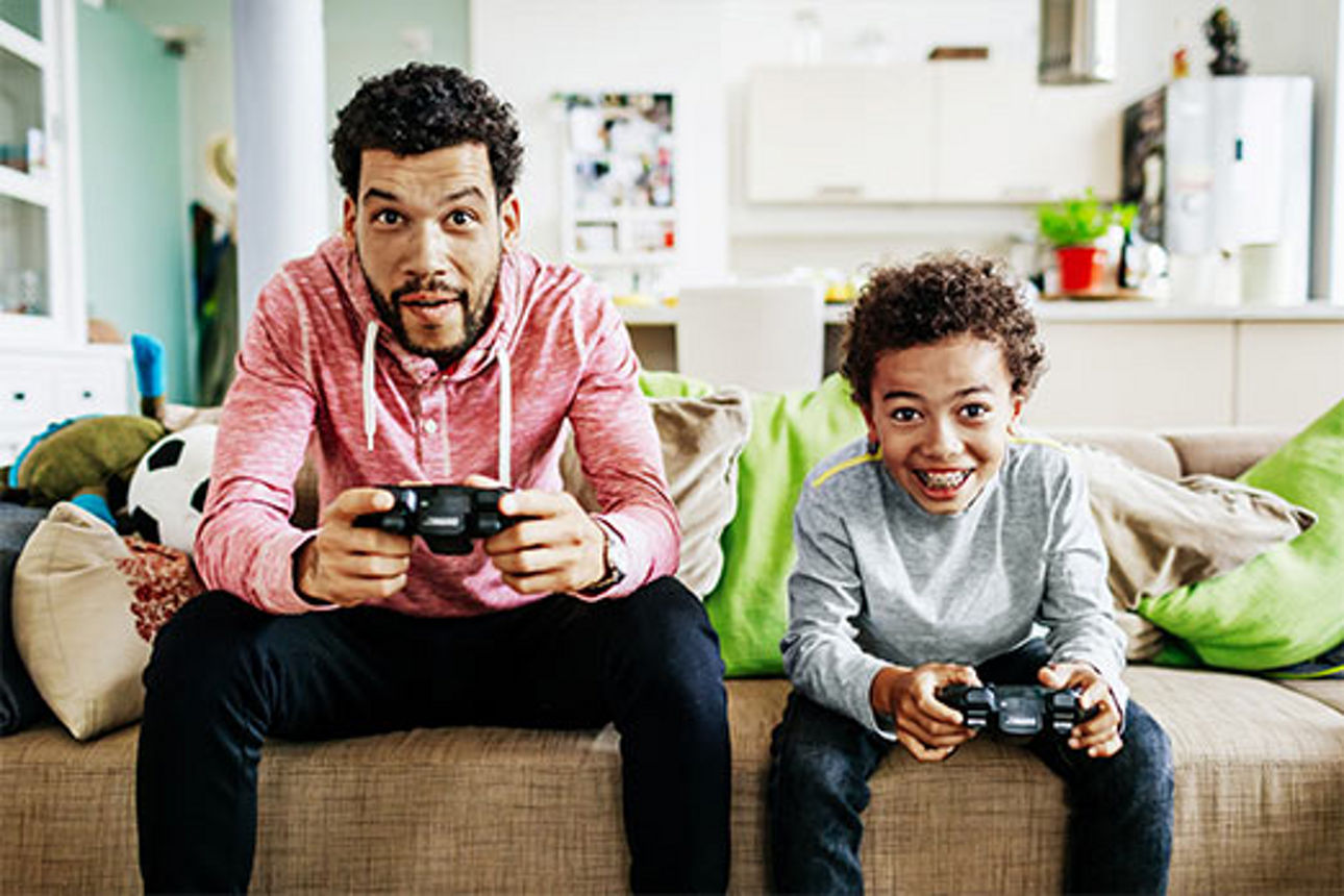 Vater und Sohn sitzen nebeneinander auf der Couch und spielen ein Videospiel