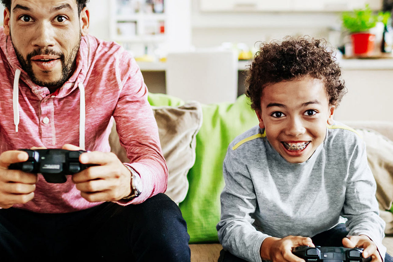Vater und Sohn sitzen nebeneinander auf der Couch und spielen ein Videospiel