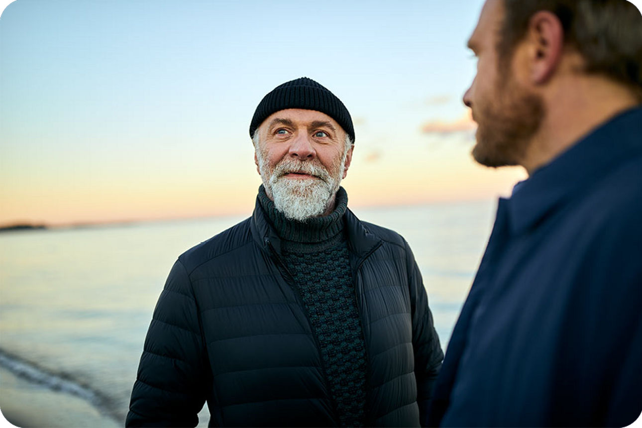 Person mit Mütze am Meer, zweite Person unscharf im Vordergrund.