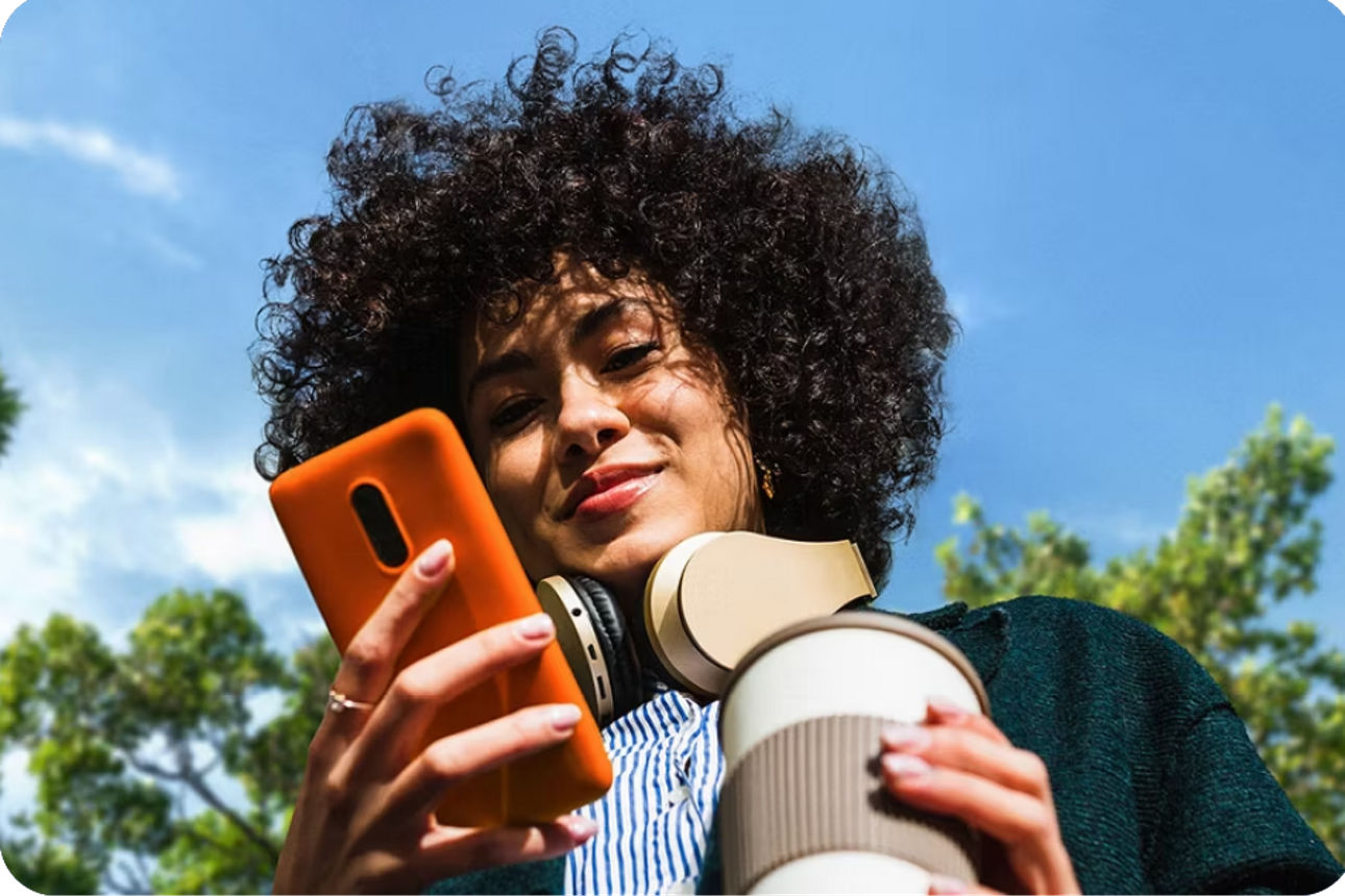 Person schaut bei strahlend blauem Himmel auf ihr Handy