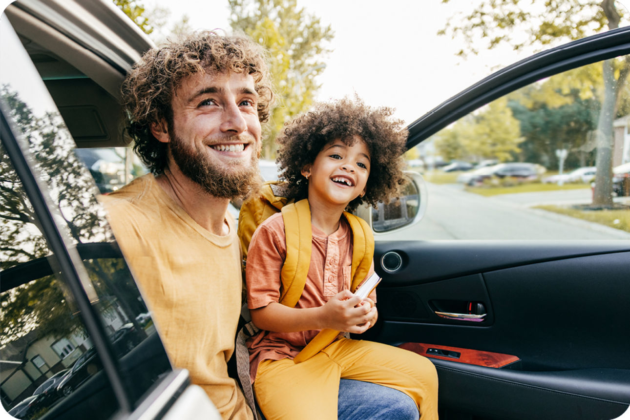 Eine erwachsene Person und ein Kind sitzen in einem geparkten Auto im Freien.