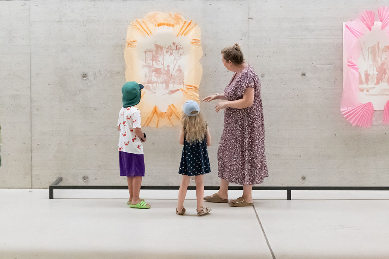 3 Kunstbilder hängen - Frau steht mit 2 Kindern vor einem Bild