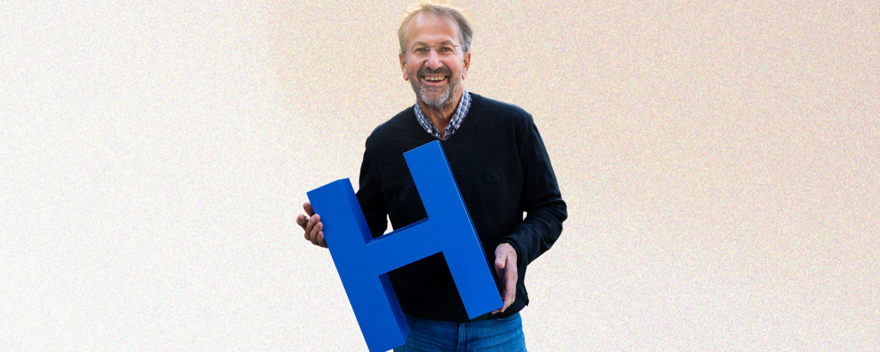 Mann hält blauen Buchstaben H in der Hand. H steht für Heimat