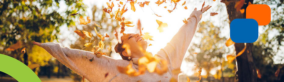 Eine Frau wirft freudig bunte Blätter in die Luft, um die Schönheit des Herbstes zu feiern.