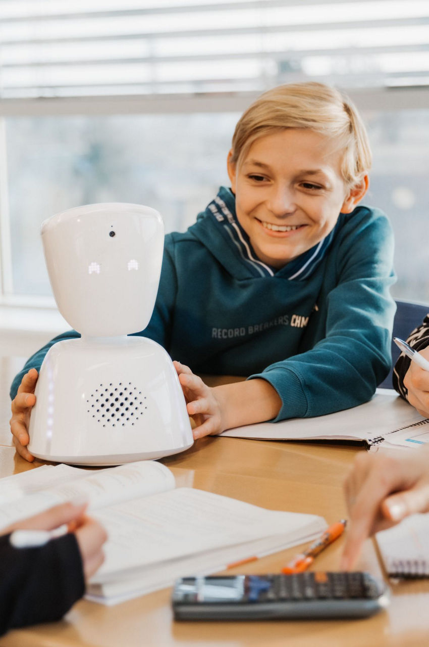 Miniroboter steht vor lächelndem Jungen auf dem Tisch