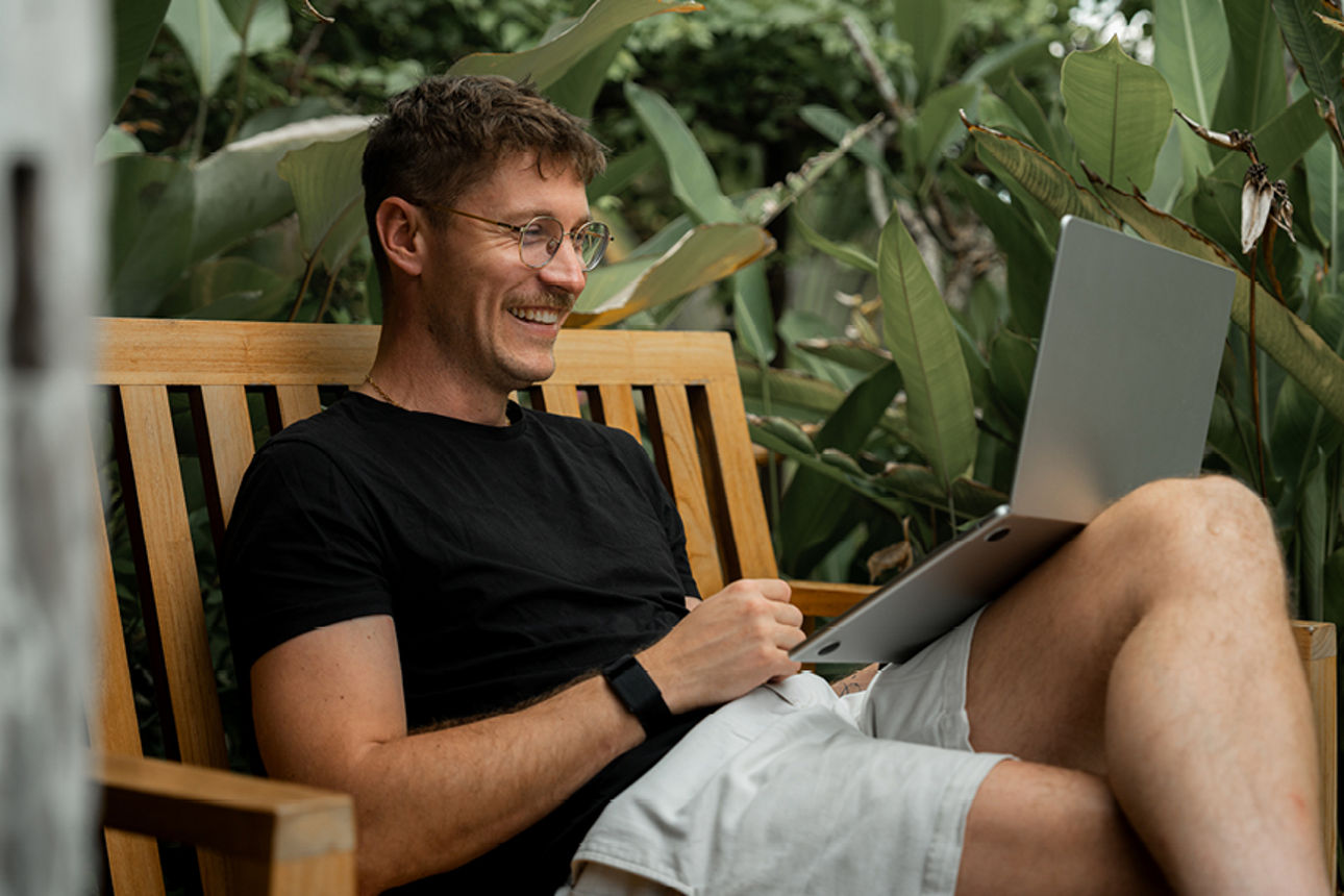 Mann sitzt mit Laptop draußen im Garten 