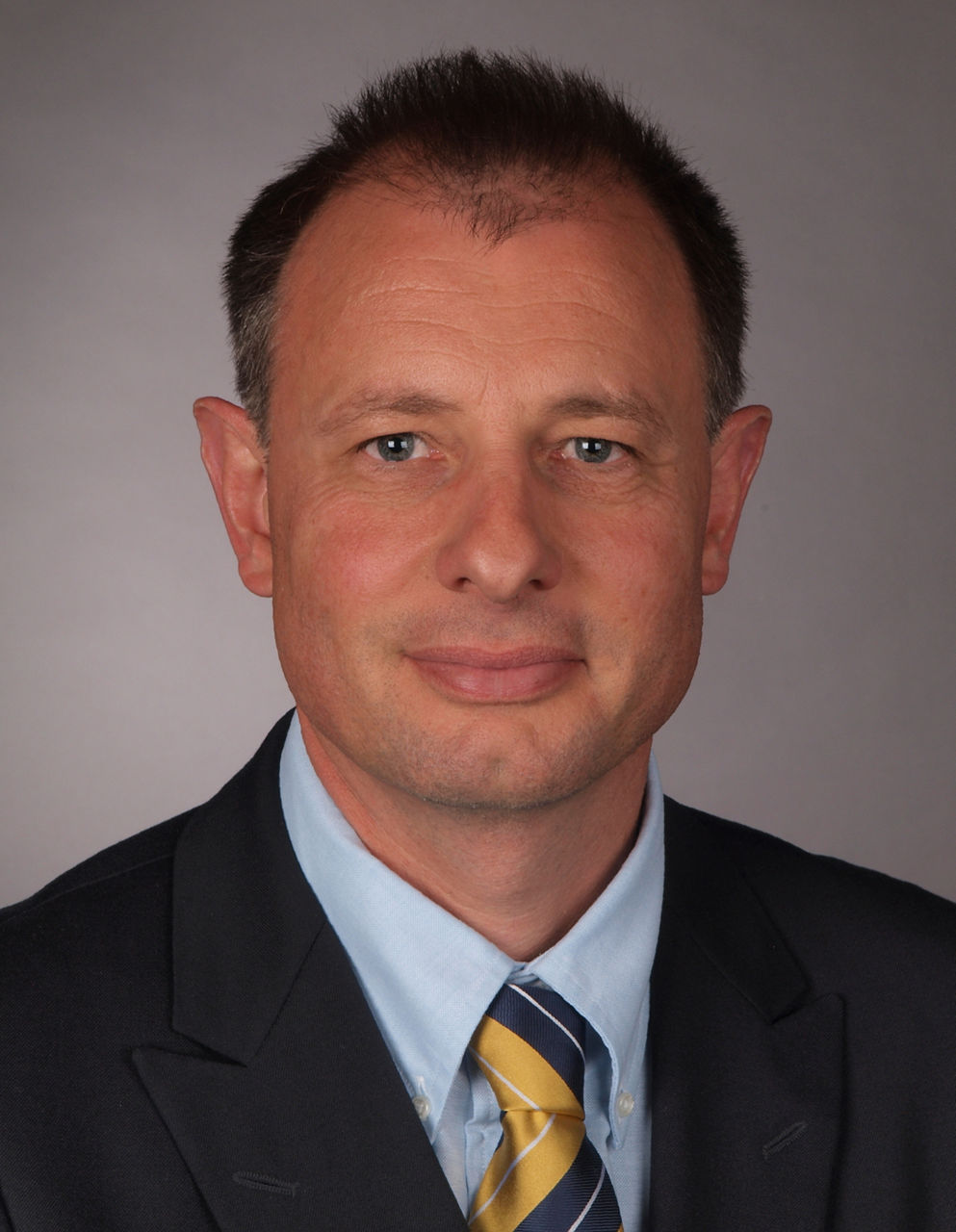 Mitarbeiter der Bank im Anzug mit gelb-blauer Krawatte lächelt in die Kamera.