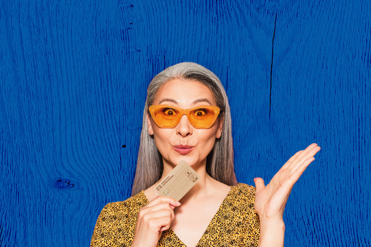 Frau in gelben Oberteil mit Holzkreditkarte in der Hand vor blauem Hintergrund