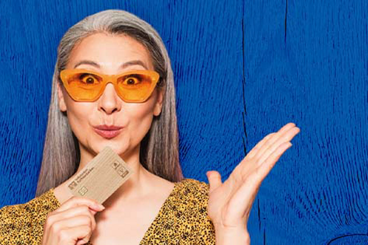 Grafik zeigt blauen Hintergrund une eine Frau mit Sonnenbrille, die die Holzkarte in der Hand hält.