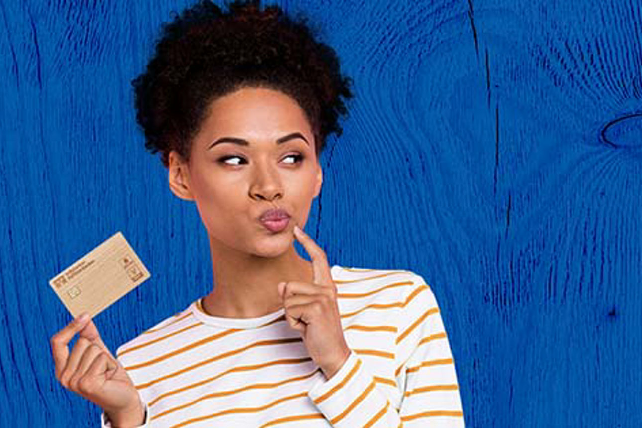 Frau im gelb weiß gestreiften Pullover mit Holzkarte in der Hand vor blauem Hintergrund