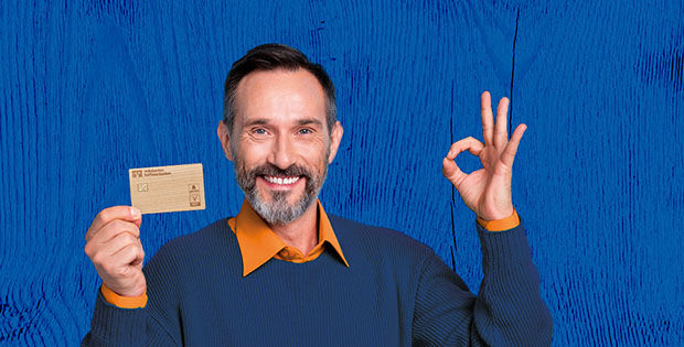 Mann im dunkelblauen Pullover mit Holzkarte in der Hand vor blauem Hintergrund