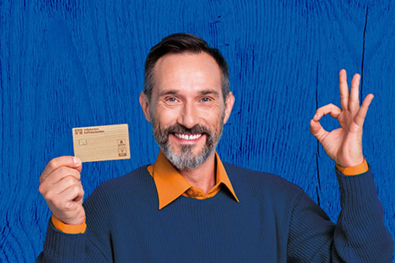 Mann im dunkelblauen Pullover mit Holzkarte in der Hand vor blauem Hintergrund