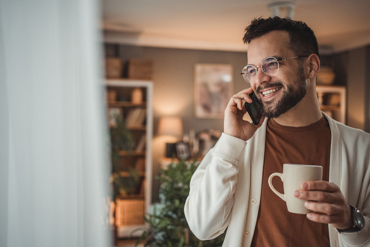 Mann telefoniert, hält einen Kaffe in der Hand und lächelt
