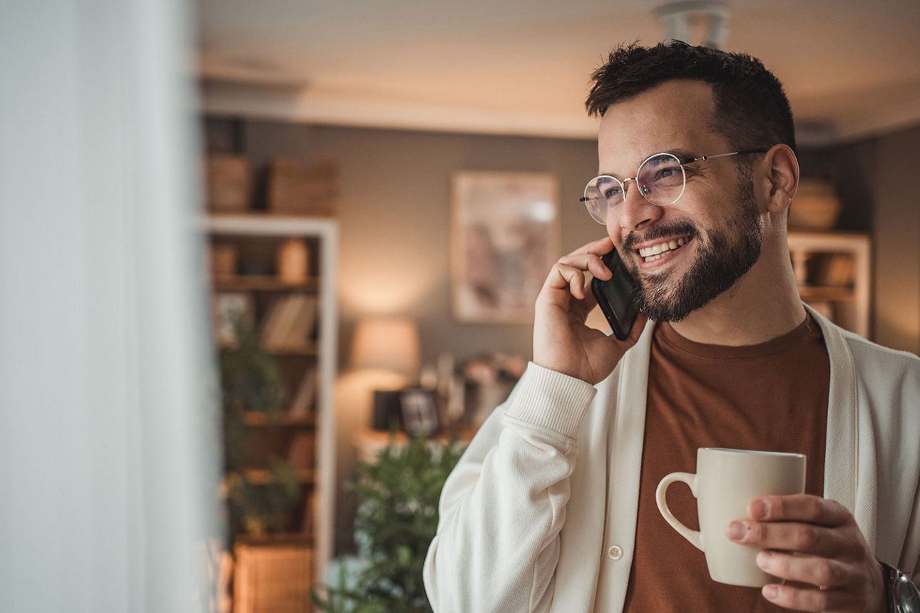Mann telefoniert, hält einen Kaffe in der Hand und lächelt