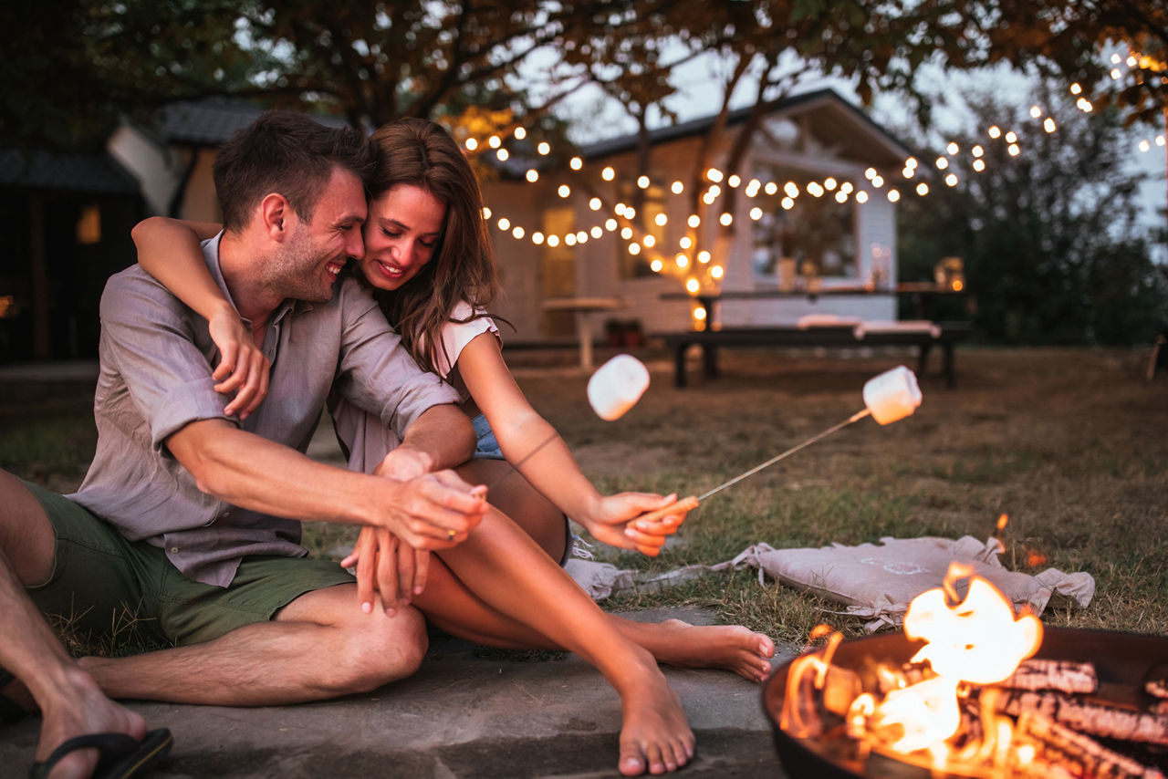 Paar umarmt sich und hält Marshmallows in ein Lagerfeuer im Garten.