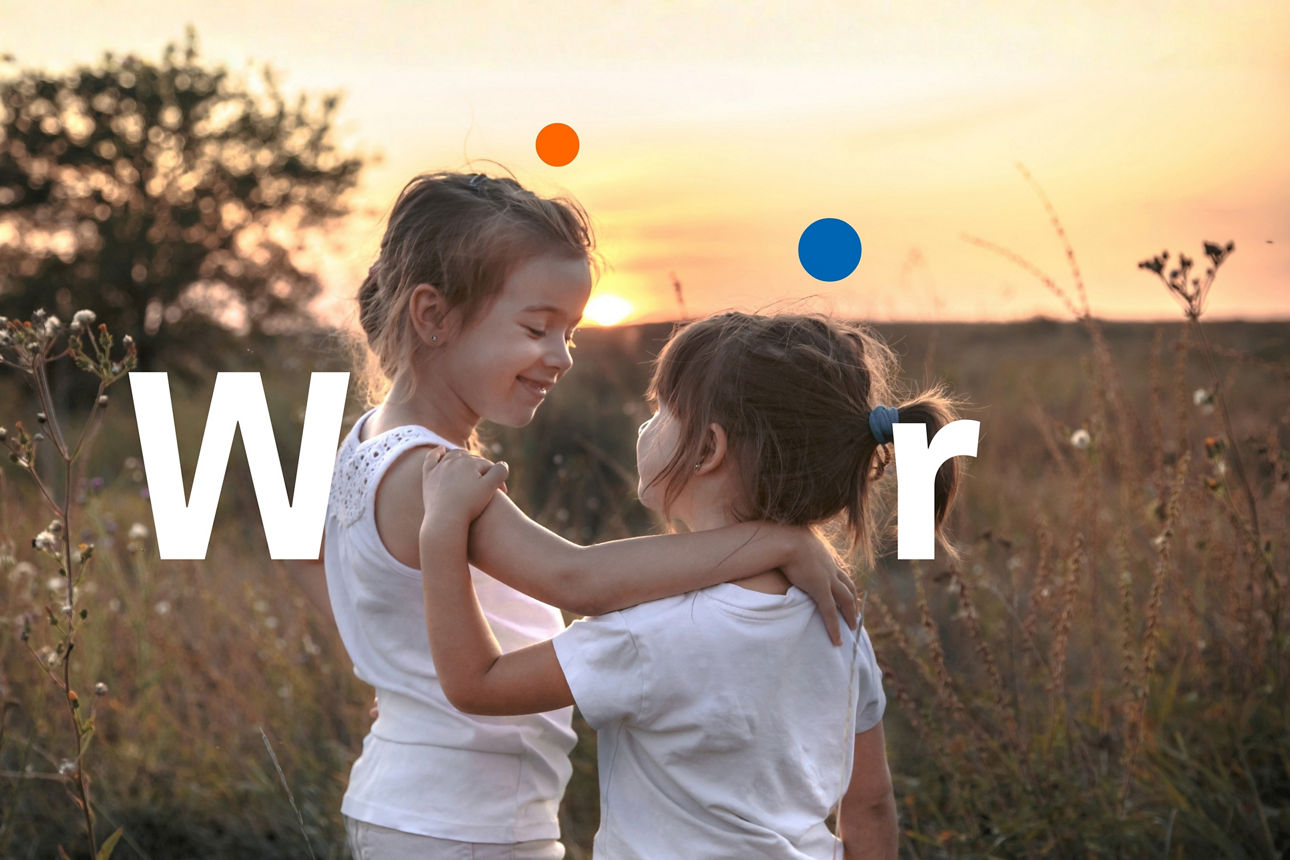 Zwei kleine Schwestern umarmen sich auf einem Feld bei Sonnenuntergang. Sie sind weiß gekleidet. Das Thema: Familienwerte und Freundschaft.