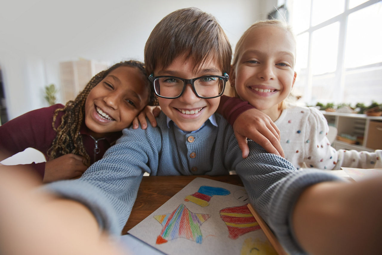 Portrait of three happy children smiling at camera while taking selfie photo in school