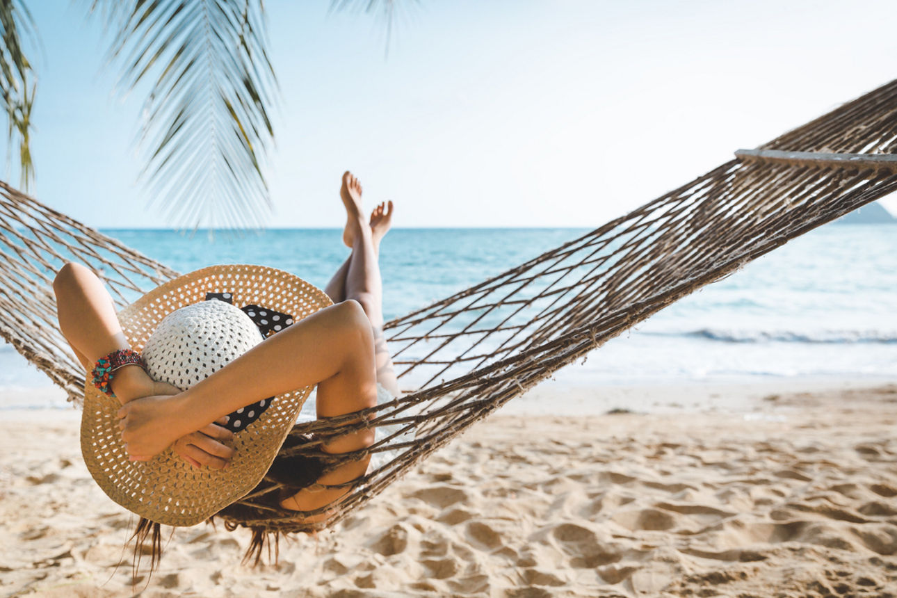 Eine Frau liegt am Strand entspannt in einer Hängematte.