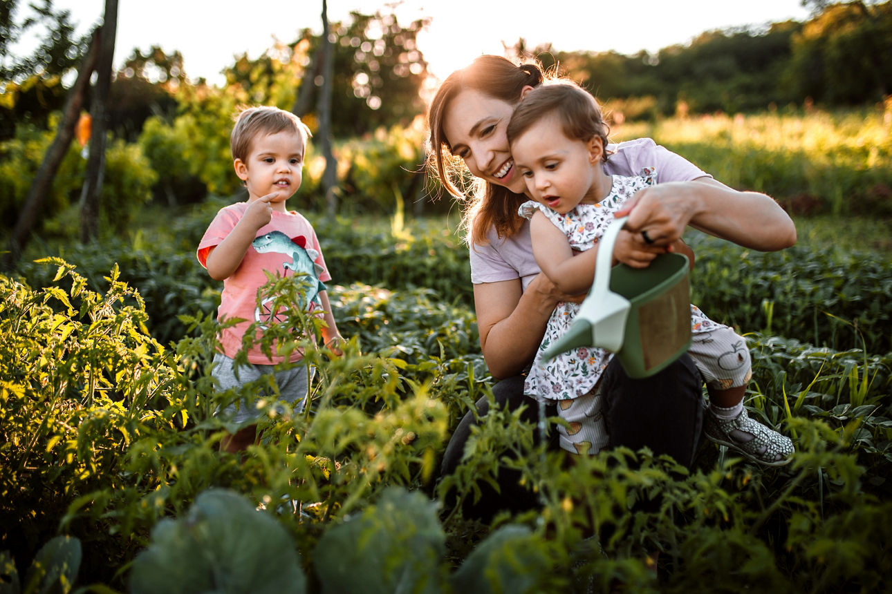 Mutter und zwei Kinder gießen Pflanzen im Garten