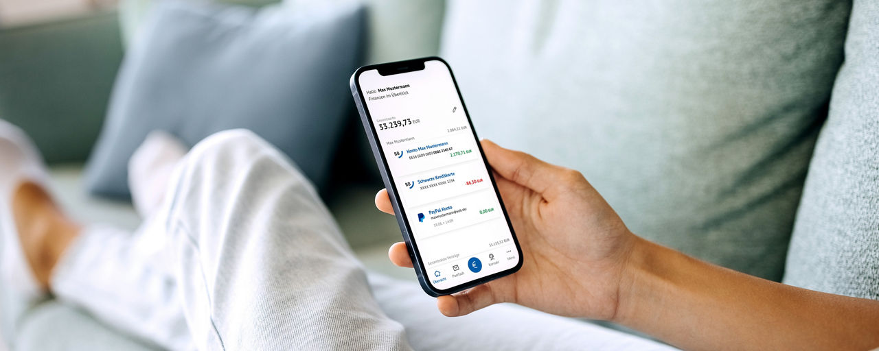 Person sitzt auf dem Sofa und hält Smartphone mit der BBBank-BankingApp vor sich