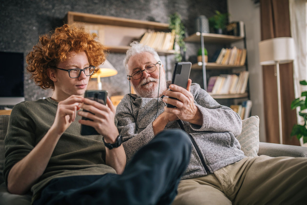 Ein junger und ein älterer Mann sitzen auf einem Sofa und schauen in ihre smartphones.