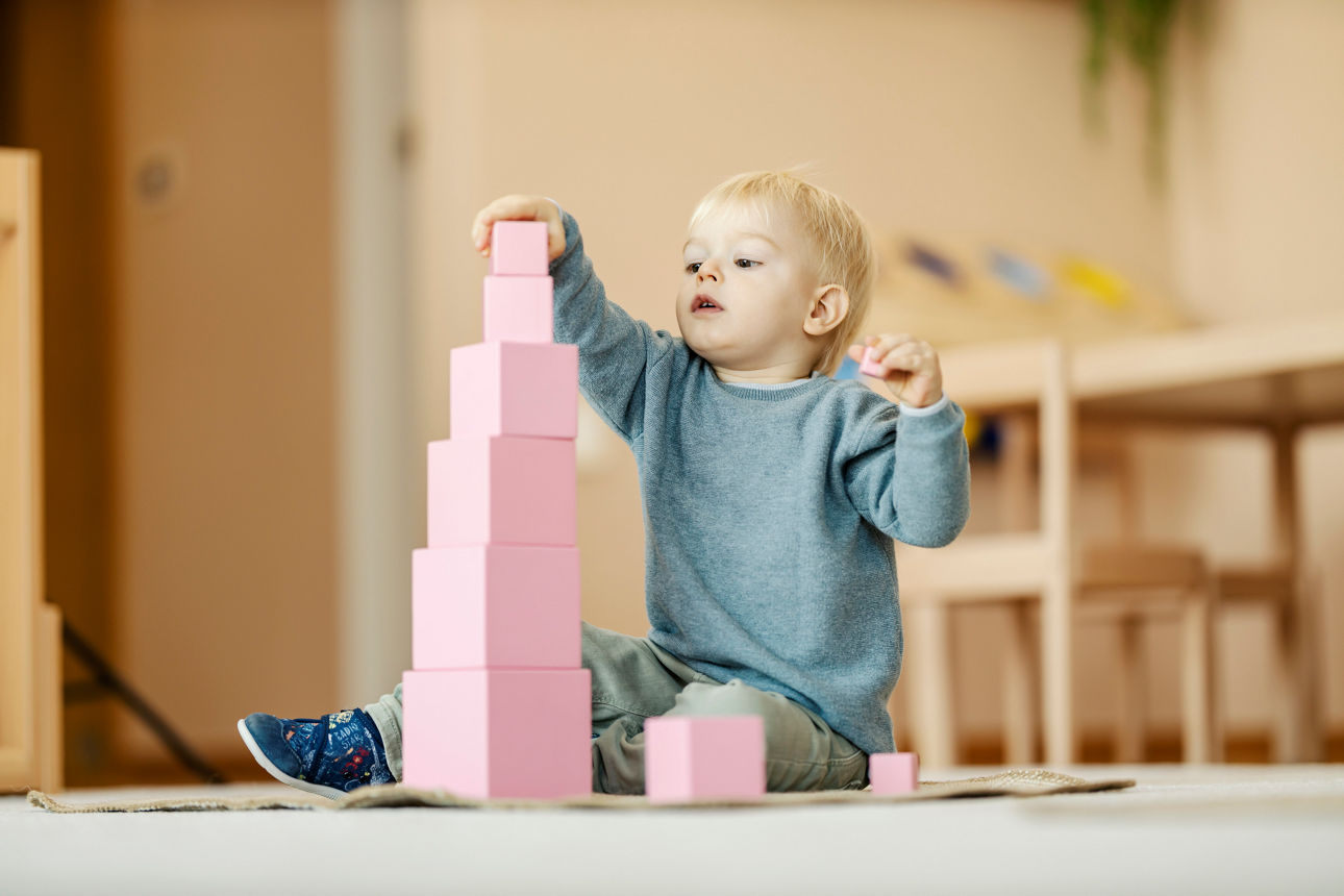 Ein ernsthafter Kindergartenschüler baut einen Turm aus Bauklötzen 