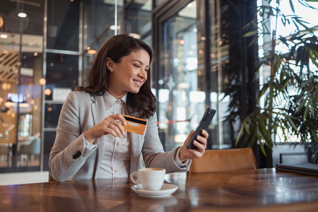 Frau sitzt im Cafe und guckt auf ihr Smartphone und hält eine Karte in der Hand.