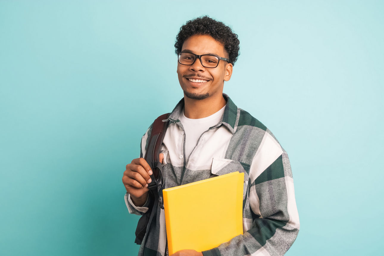Glücklicher männlicher Universitätsstudent mit Rucksack und Büchern im blauen Studio