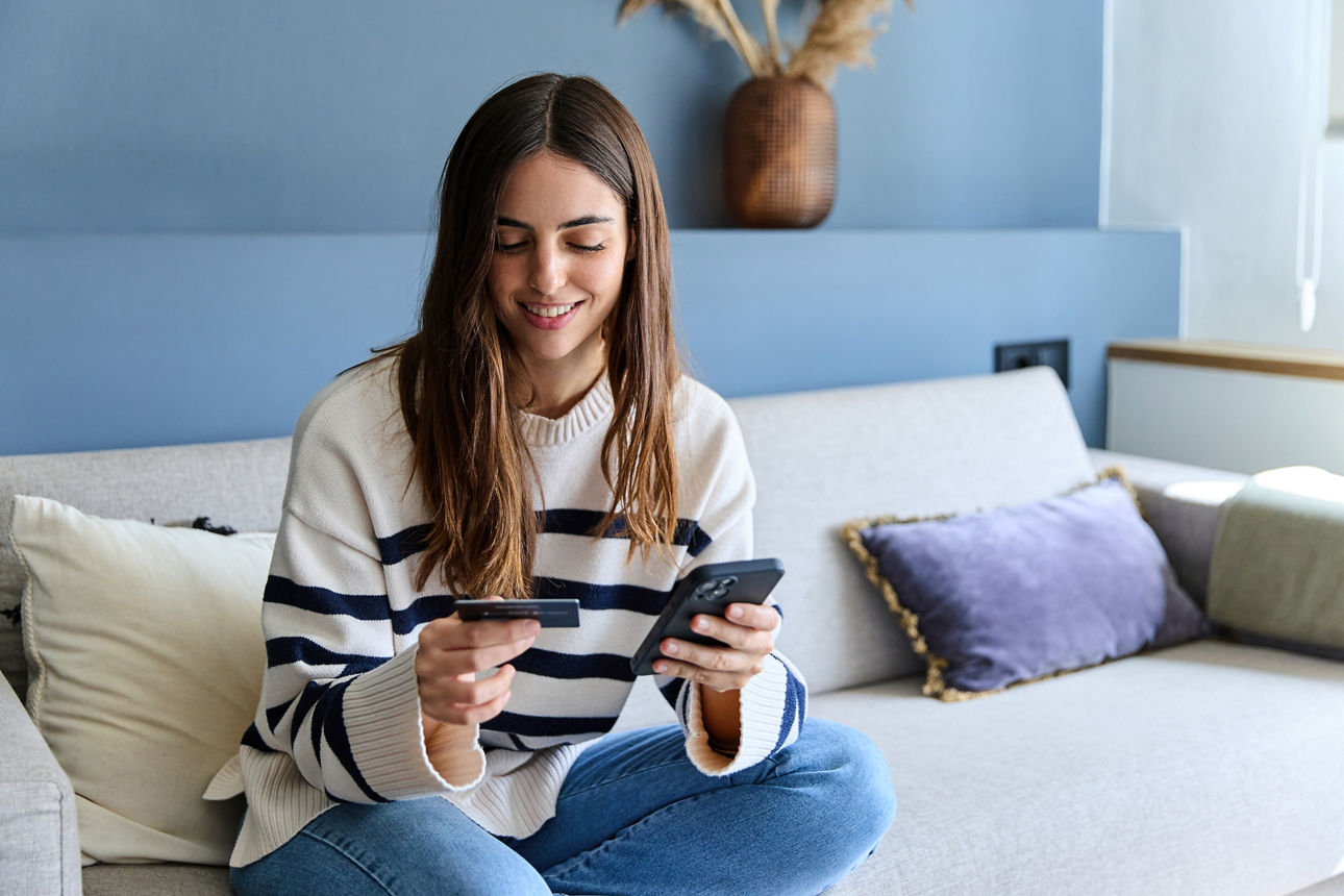 Lächelnde Frau, die zu Hause online mit Kreditkarte und Smartphone bezahlt