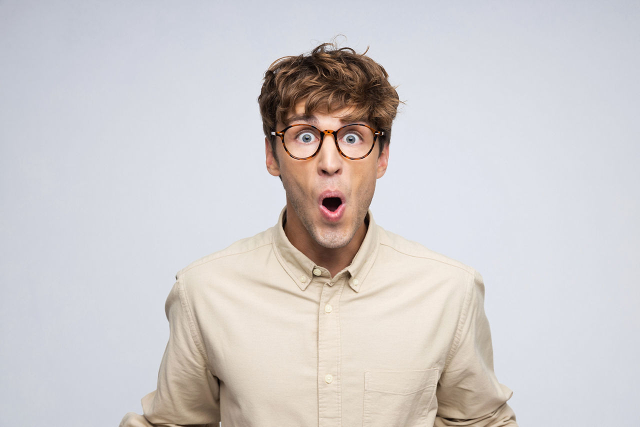 Portrait eines jungen Mannes in beigefarbenem Hemd, der mit staunendem Blick in die Kamera schaut.