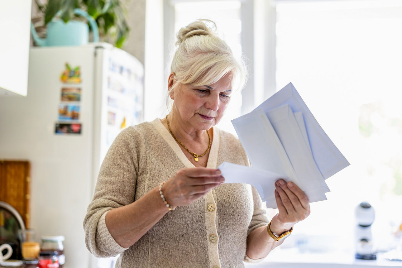 Seniorin liest ihre Post und Dokumente in der Küche.