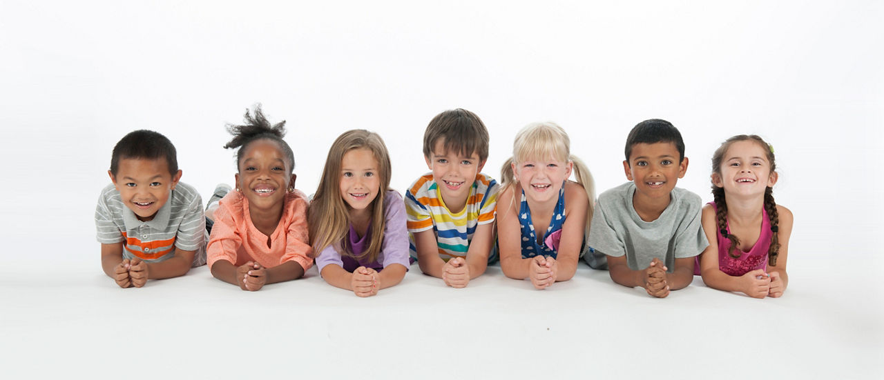 Eine Gruppe Kinder aller Ethnien liegen auf die Arme gestützt am Boden.