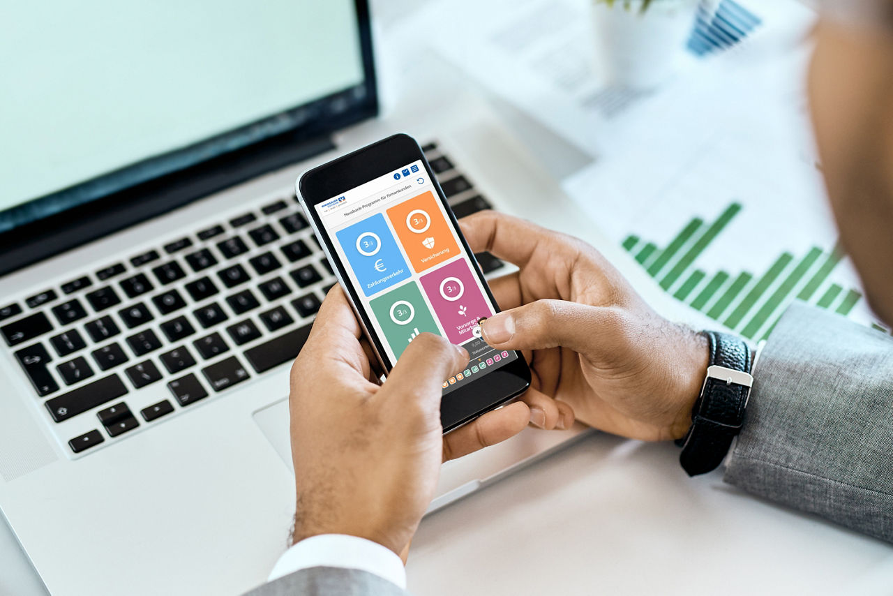 Eine Person hat ein Handy in der Hand und schaut sich die Bausteine des Hausbankprogramms an