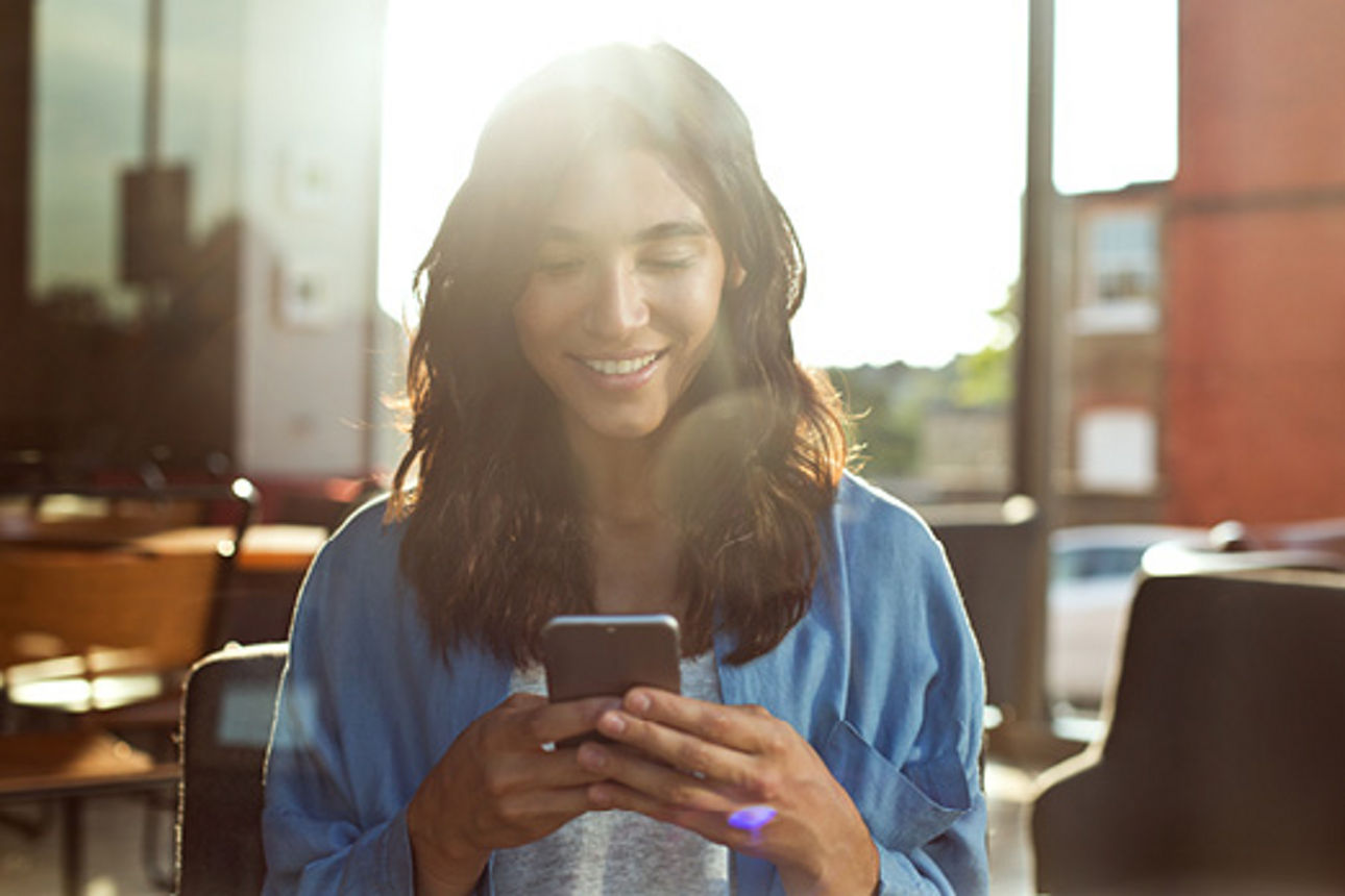 Junge Frau schaut auf ihr Handy und freut sich