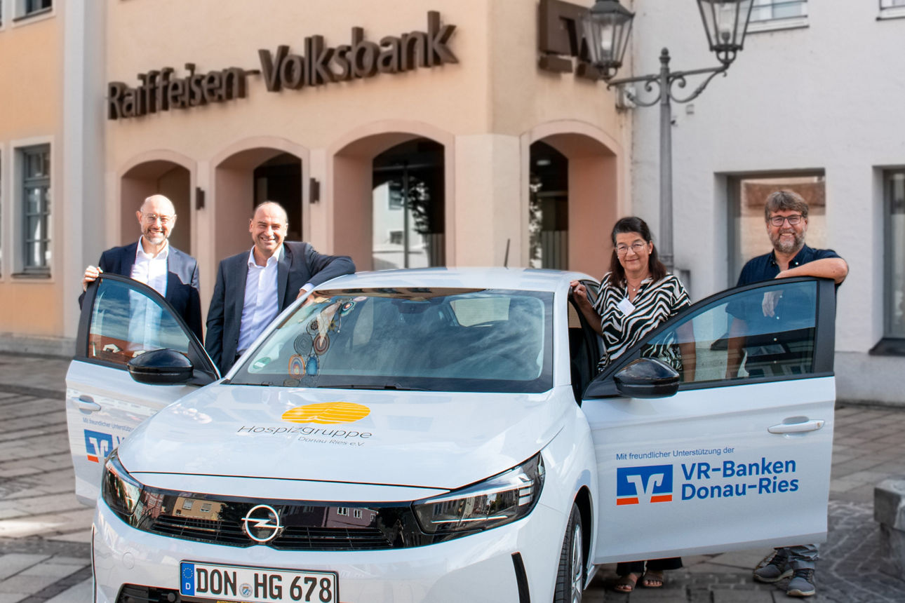 Vier Personen stehen neben einem Fahrzeug vor einem Bankgebäude.