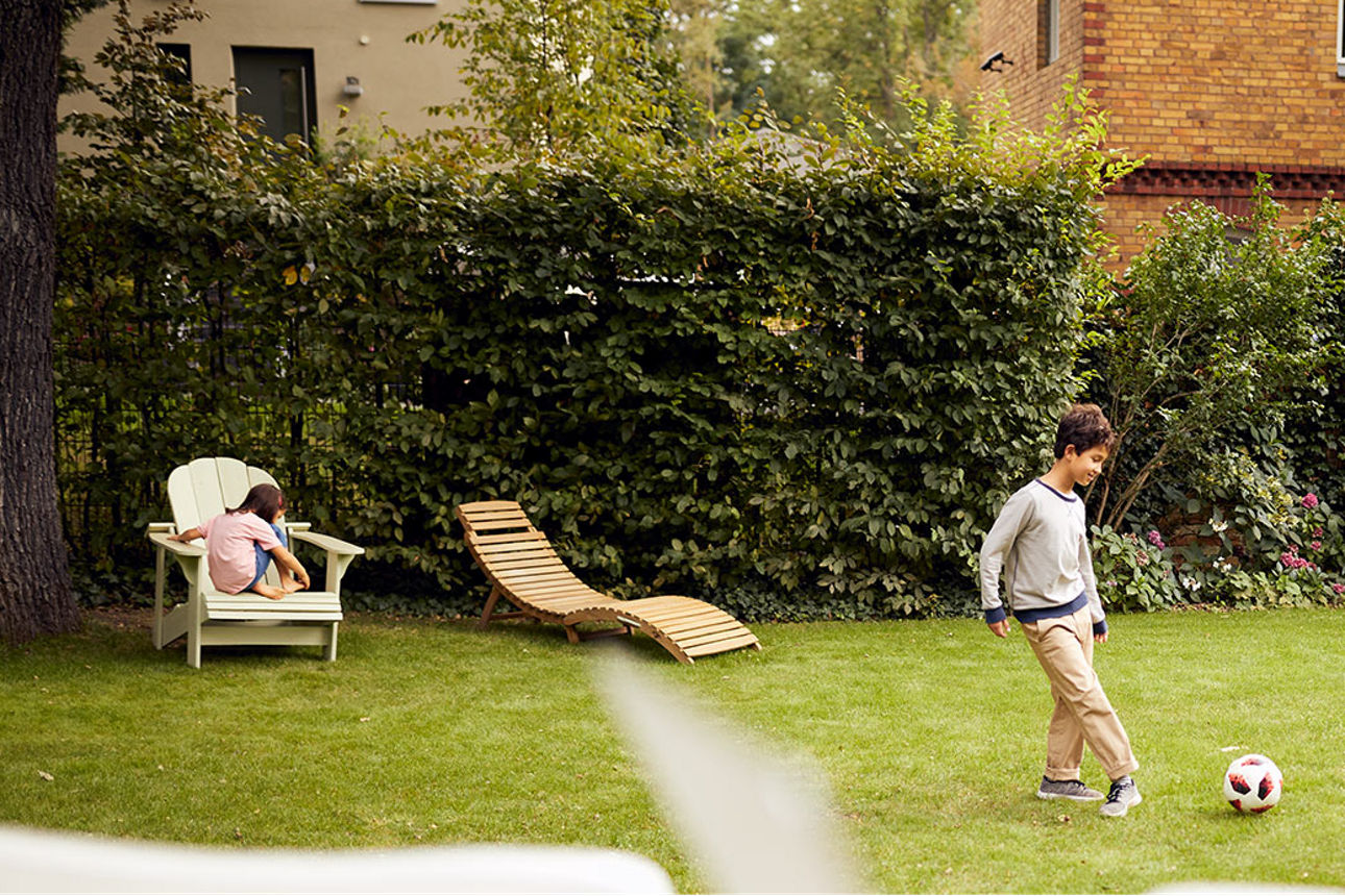 Frau bei Online-Recherche zur Immobilienbewertung mit Familie im Garten