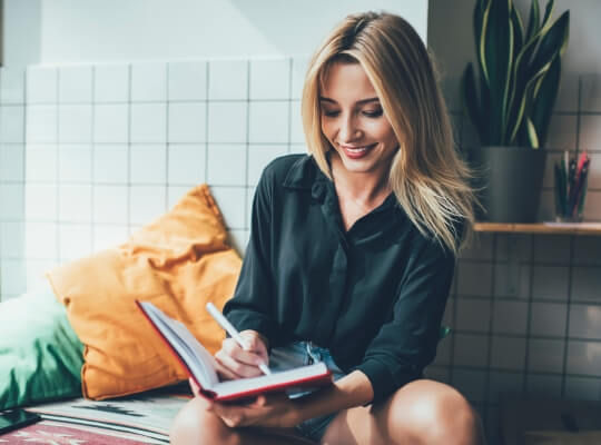 Eine junge Frau mit einem Stift und einem Notizbuch in der Hand prüft ihre Einträge.
