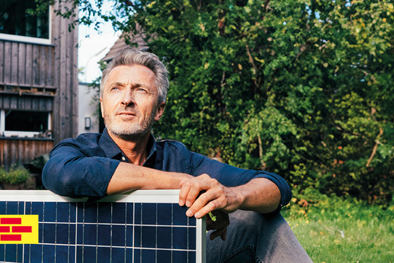 Ein Mann mit Bart steht vor einem Gerüst und lächelt in die Kamera