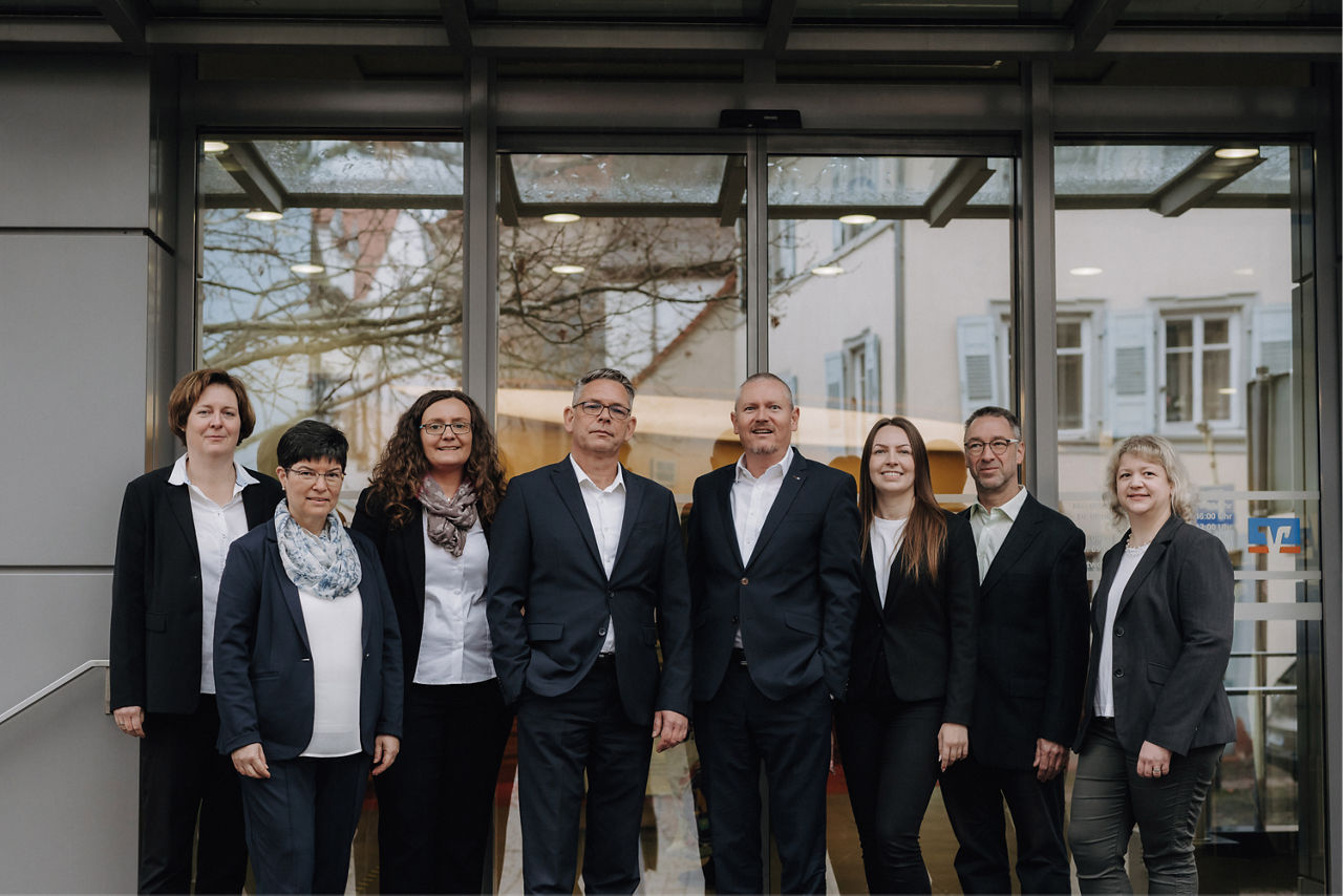 Eine Gruppe vopn Männern und Frauen in Anzügen vor einer Glasfront.
